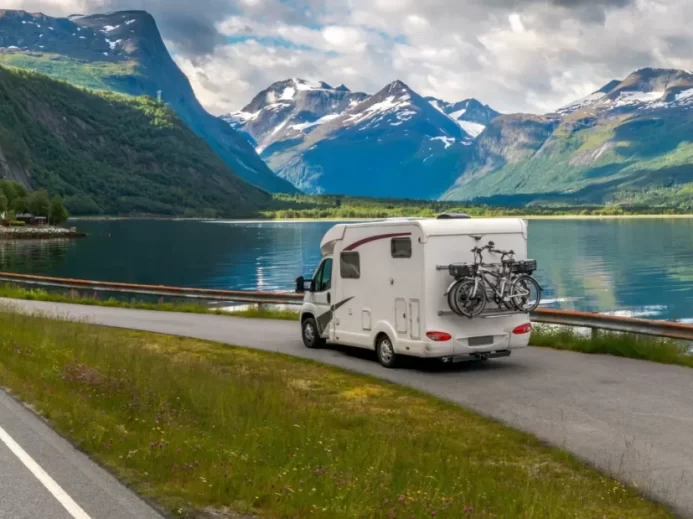Obytný vůz parkuje u klidného fjordu obklopeného horami, s koly připevněnými na zadní straně