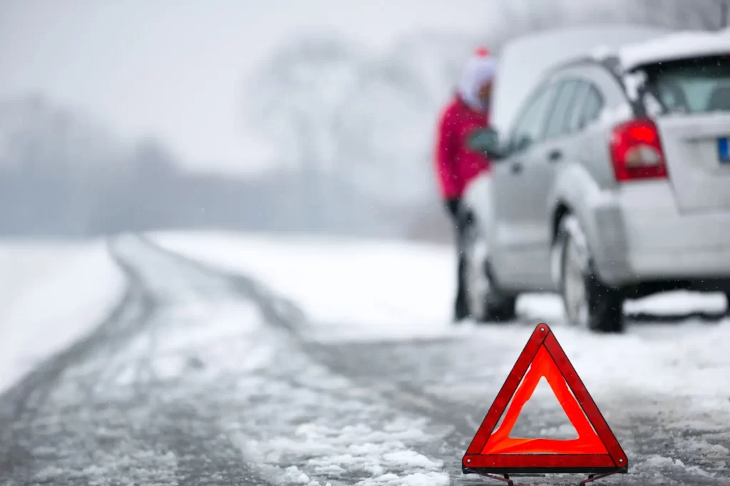 Porouchané auto na zimní silnici. Výstražný trojúhelník v popředí