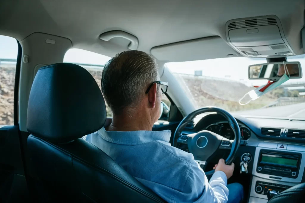 Starší muž řídí běžné auto, pohled zezadu