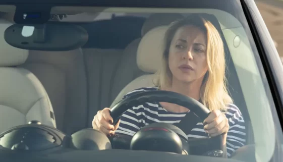 Blond žena za volantem kontroluje, zda má na silnici volno.