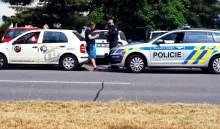 Policista právě kontroluje doklady řidiče bílého služebního vozu s logem TD servis, zatímco policejní vozidlo stojí zaparkované hned vedle.