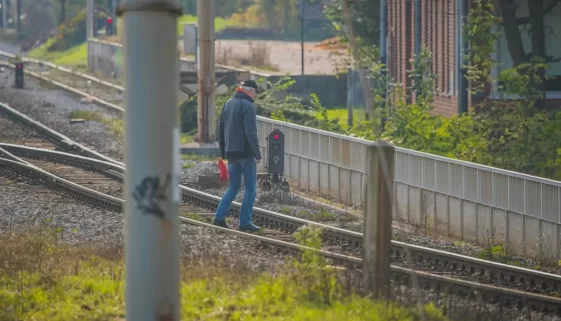 Muž přechází kolejiště když svítí červené světlo