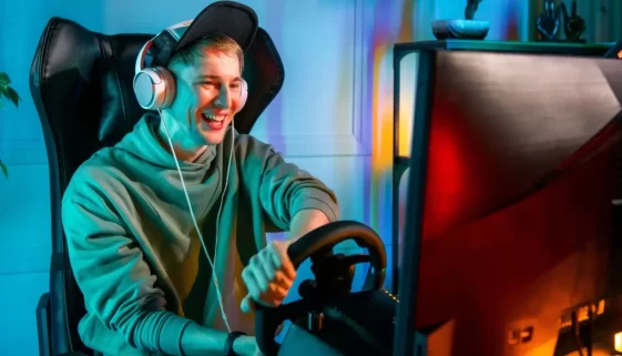 MLadý muž sedí u počítače se sluchátky na uších a drží volant