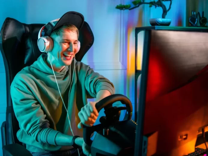 MLadý muž sedí u počítače se sluchátky na uších a drží volant