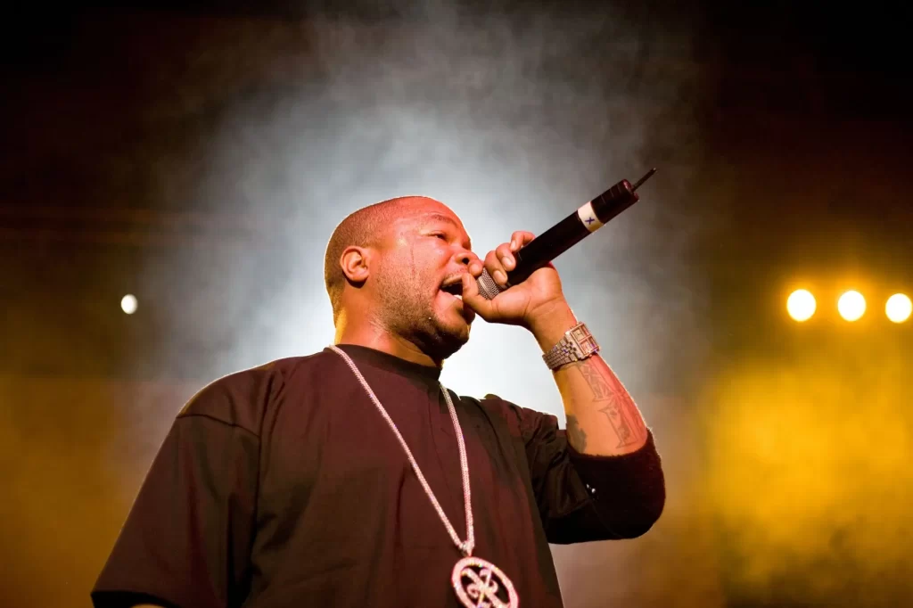 Rapper Xzibit při koncertním vystoupení. Má mikrofon v ruce, výrazný řetěz na krku.