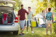 skupina mladých lidí vybaluje auto v kempu