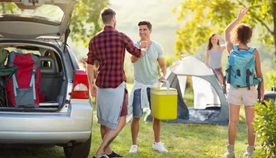skupina mladých lidí vybaluje auto v kempu