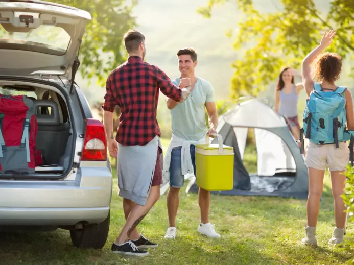 skupina mladých lidí vybaluje auto v kempu