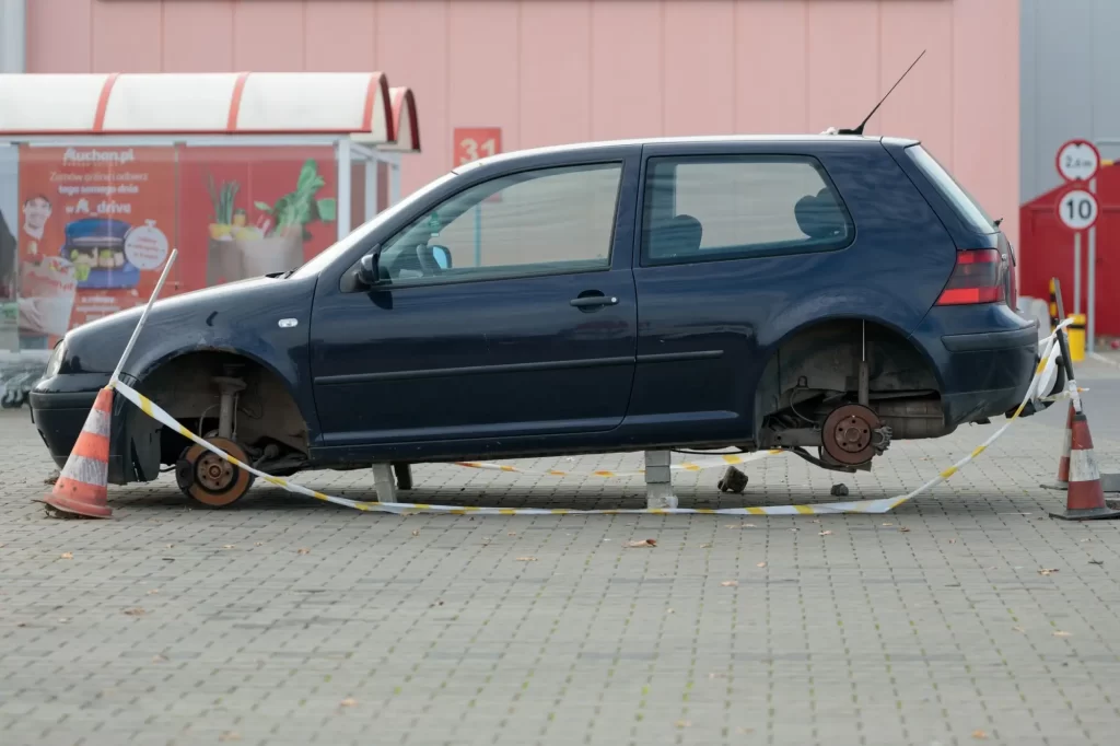 Opuštěné osobní vozidlo (Volkswagen Golf), odstavené na parkovišti bez kol, podložené betonovými bloky.