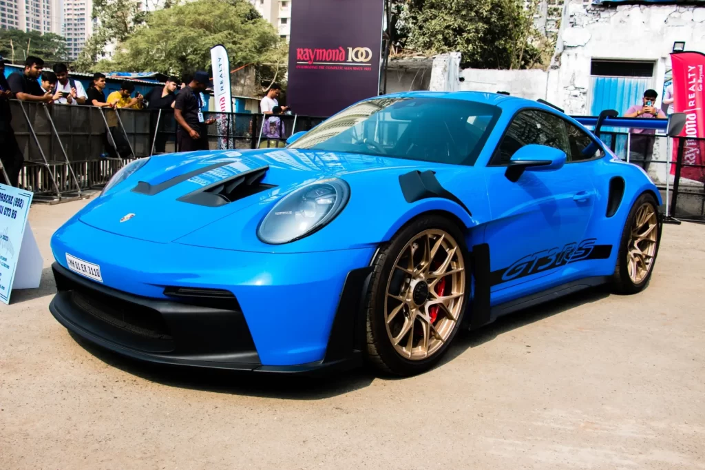 Porsche 911 GT3 RS (992) v jasně modré barvě s černými aerodynamickými prvky a zlatými litými koly. 