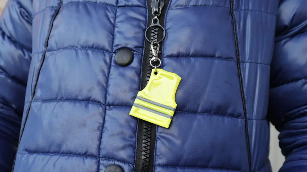 Záběr na modrou prošívanou bundu, na jejímž zipu visí malý přívěsek ve tvaru reflexní vesty.