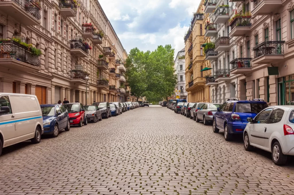 - MotorGuru.cz Evropská městská ulice s dlažebními kostkami a zaparkovanými auty po obou stranách.