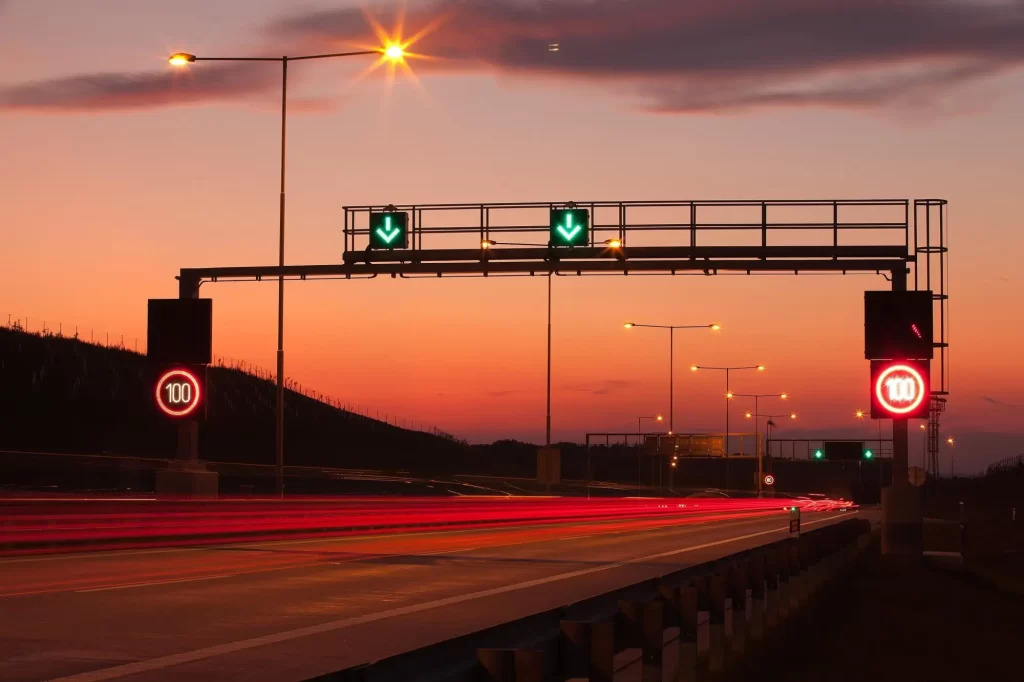 - MotorGuru.cz Moderní dálniční úsek za soumraku, osvětlený pouličními lampami a digitálními dopravními značkami.
