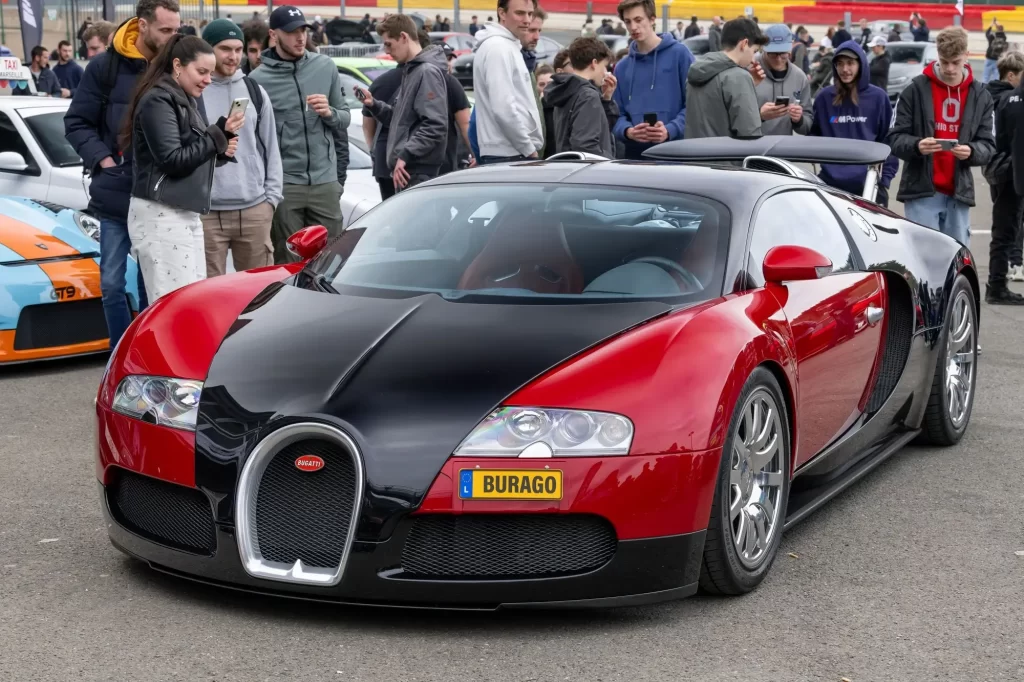 Bugatti Veyron v lesklé dvoubarevné kombinaci černé a červené, vystavený na automobilové akci za účasti mnoha diváků.