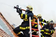Hasiči stojí s hadicí na sgtřeše a hasí požár
