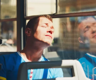 Muž sedí v tramvaji a sluní se přes okno