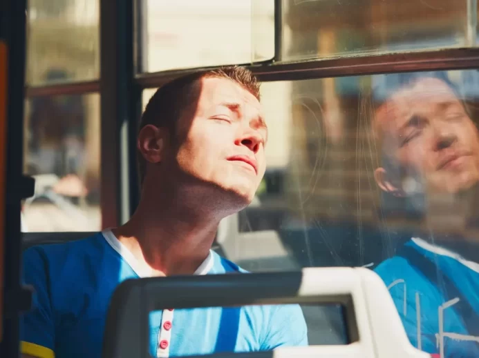 Muž sedí v tramvaji a sluní se přes okno