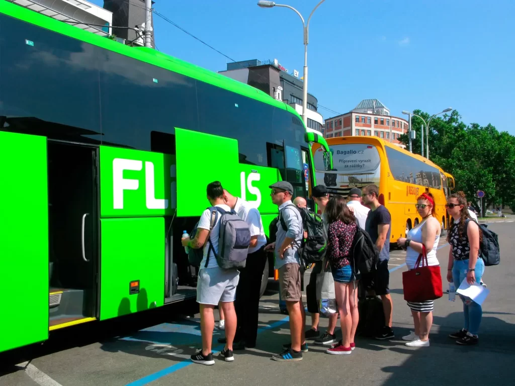 Skupina lidí ve frontě na nástup do zeleného dálkového autobusu FlixBus. 