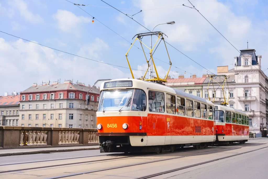 Klasická červeno-bílá tramvaj typu Tatra T3 projíždějící po pražských kolejích přes most.
