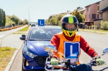 Student auroškoly na motorce, za ním auto autoškoly