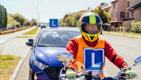 Student auroškoly na motorce, za ním auto autoškoly