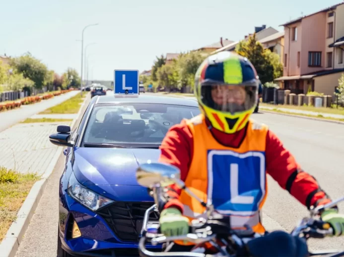Student auroškoly na motorce, za ním auto autoškoly