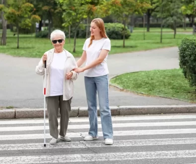 Žena převádí nevidomou osobu přes přechod