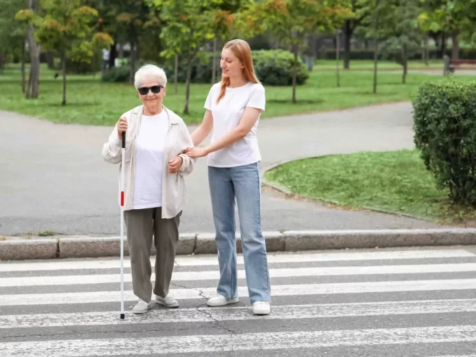 Žena převádí nevidomou osobu přes přechod