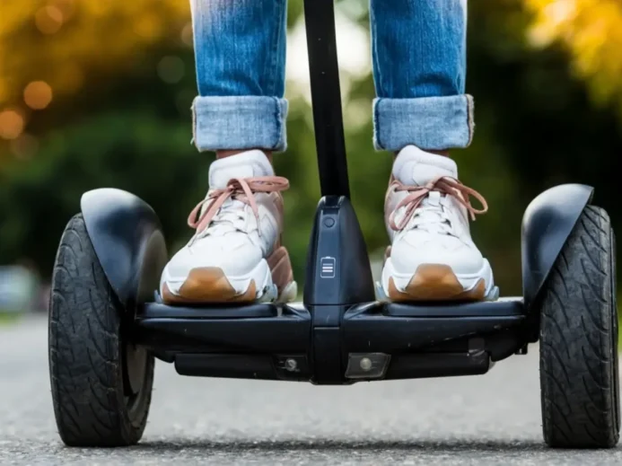 Pohled zblízka na boty jezdce stojícího na Segwayi při jízdě po asfaltu