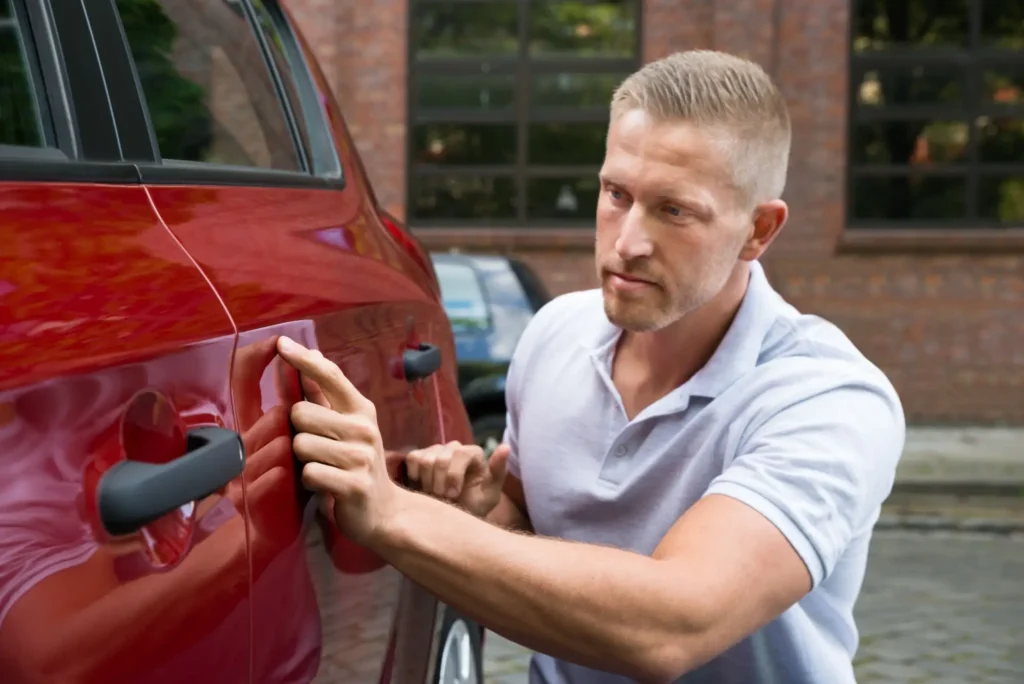 - MotorGuru.cz Muž si důkladně prohlíží karoserii červeného auta, aby odhalil případné skryté vady při koupi ojetého vozu.