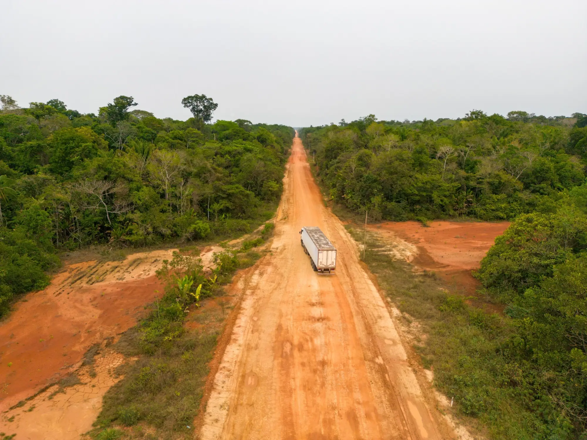 - MotorGuru.cz Nákladní vůz na prašné silnici BR-319 obklopené amazonským pralesem v Brazílii, pohled z ptačí perspektivy.