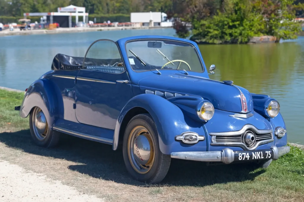 Modrý kabriolet Panhard Dyna X z poloviny 20. století, zaparkovaný u vodní plochy.