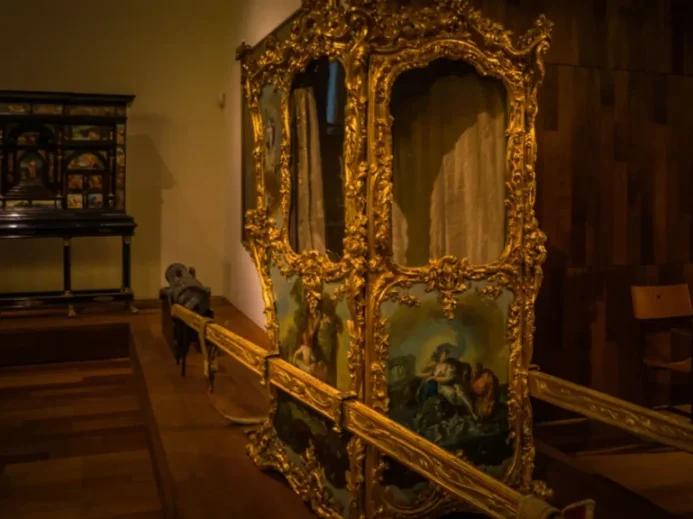 Luxusní historické nosítko s bohatou zlatou výzdobou a malovanými panely v muzeu