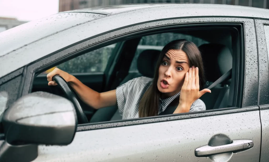 MLadá žena za volantem naštvaně gestikuluje u okénka vozu