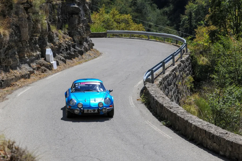 Klasické modré rallye auto projíždějící ostrou zatáčku na úzké horské silnici Col de Turini. 