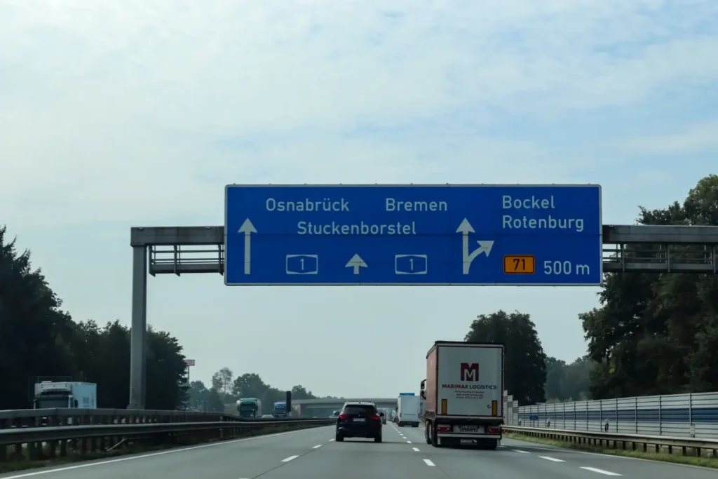 Pohled na rušnou dálnici A1 v Německu se směrovými tabulemi a projíždějícími auty