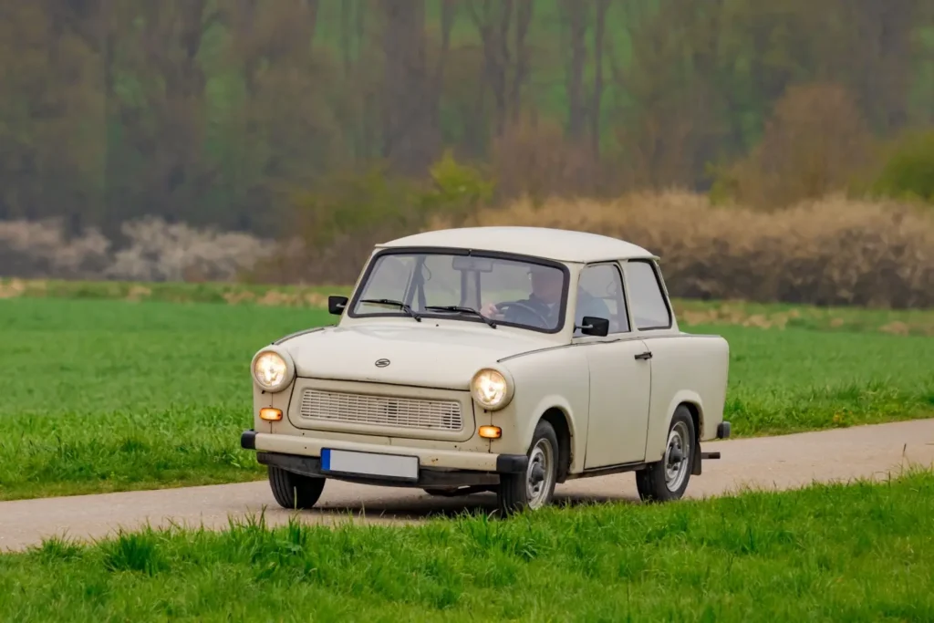 Bílý Trabant 601 projíždí venkovskou silnicí