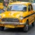 Ikonické žluté taxi typu Hindustan Ambassador, jedoucí po městské silnici v Indii.