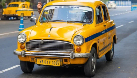Ikonické žluté taxi typu Hindustan Ambassador, jedoucí po městské silnici v Indii.