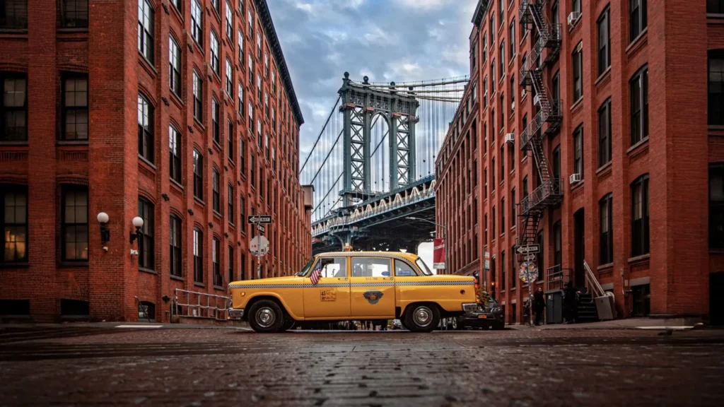 Klasický žlutý newyorský taxík Checker Marathon zaparkovaný mezi dvěma červenými cihlovými budovami v ikonické čtvrti DUMBO v Brooklynu.