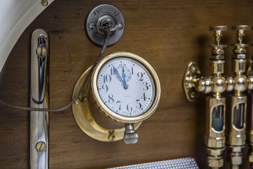 Detailní pohled na palubní hodiny a mosazné součásti interiéru vozu Laurin & Klement BSC z roku 1908