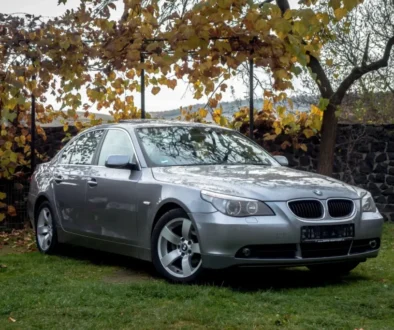 BMW řady 5 E60 zaparkované na trávníku pod stromy v podzimní krajině