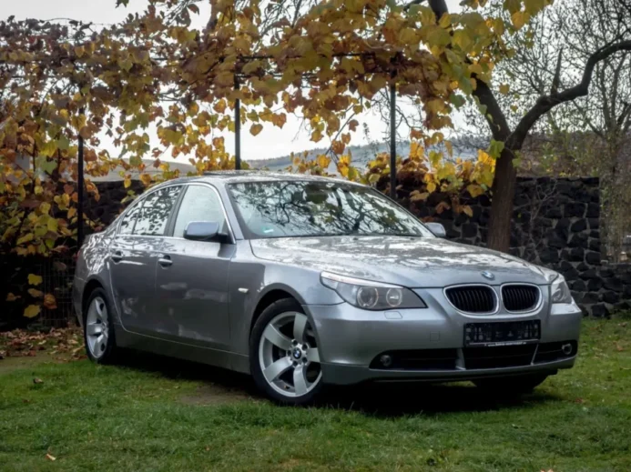 Luxus na pohled, starost v realitě BMW řady 5 E60 zaparkované na trávníku pod stromy v podzimní krajině