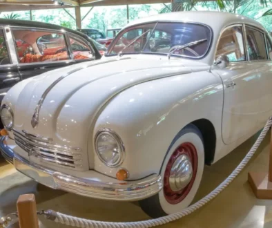 Bílý osobní automobil Tatra 600 vystavený v muzeu, obklopený dalšími historickými vozy