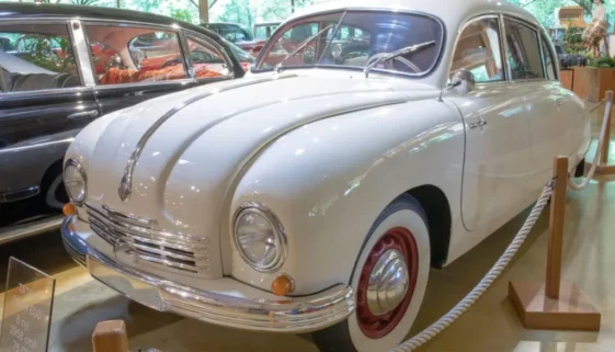 Bílý osobní automobil Tatra 600 vystavený v muzeu, obklopený dalšími historickými vozy