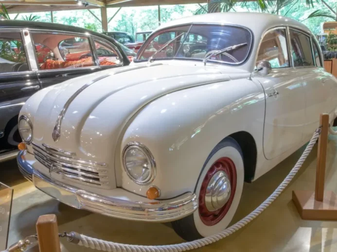 Bílý osobní automobil Tatra 600 vystavený v muzeu, obklopený dalšími historickými vozy