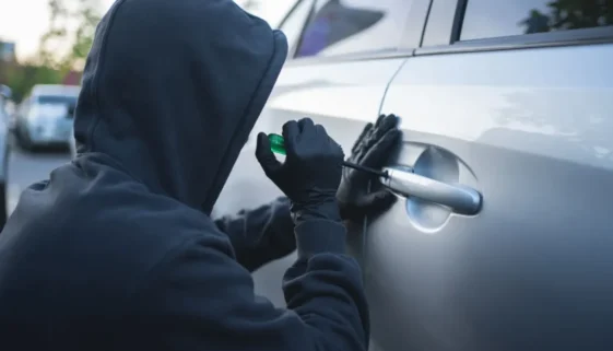 Muž v kapuci se pokouší vniknout do zaparkovaného auta na parkovišti