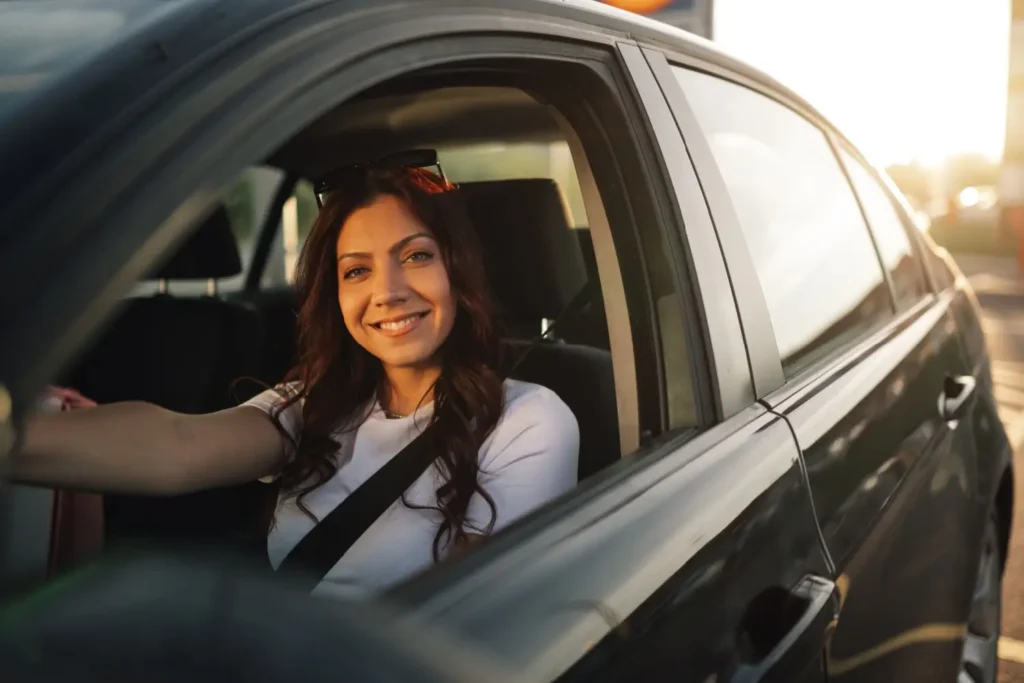 - MotorGuru.cz Žena sedí v autě a usmívá se, zatímco drží volant