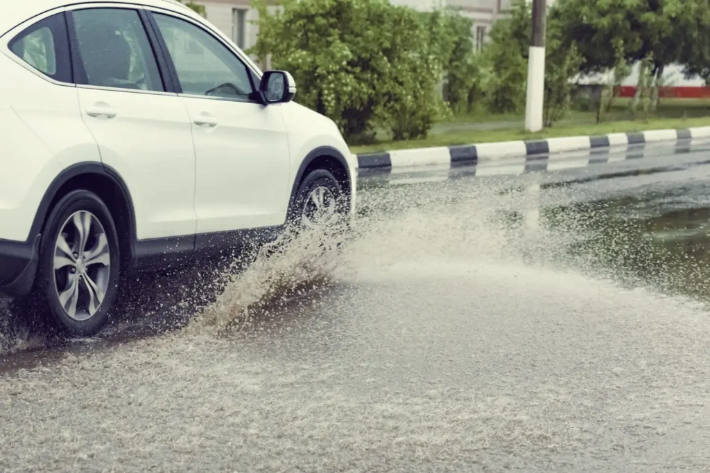 - MotorGuru.cz Bílý automobil projíždějící kaluží na mokré silnici