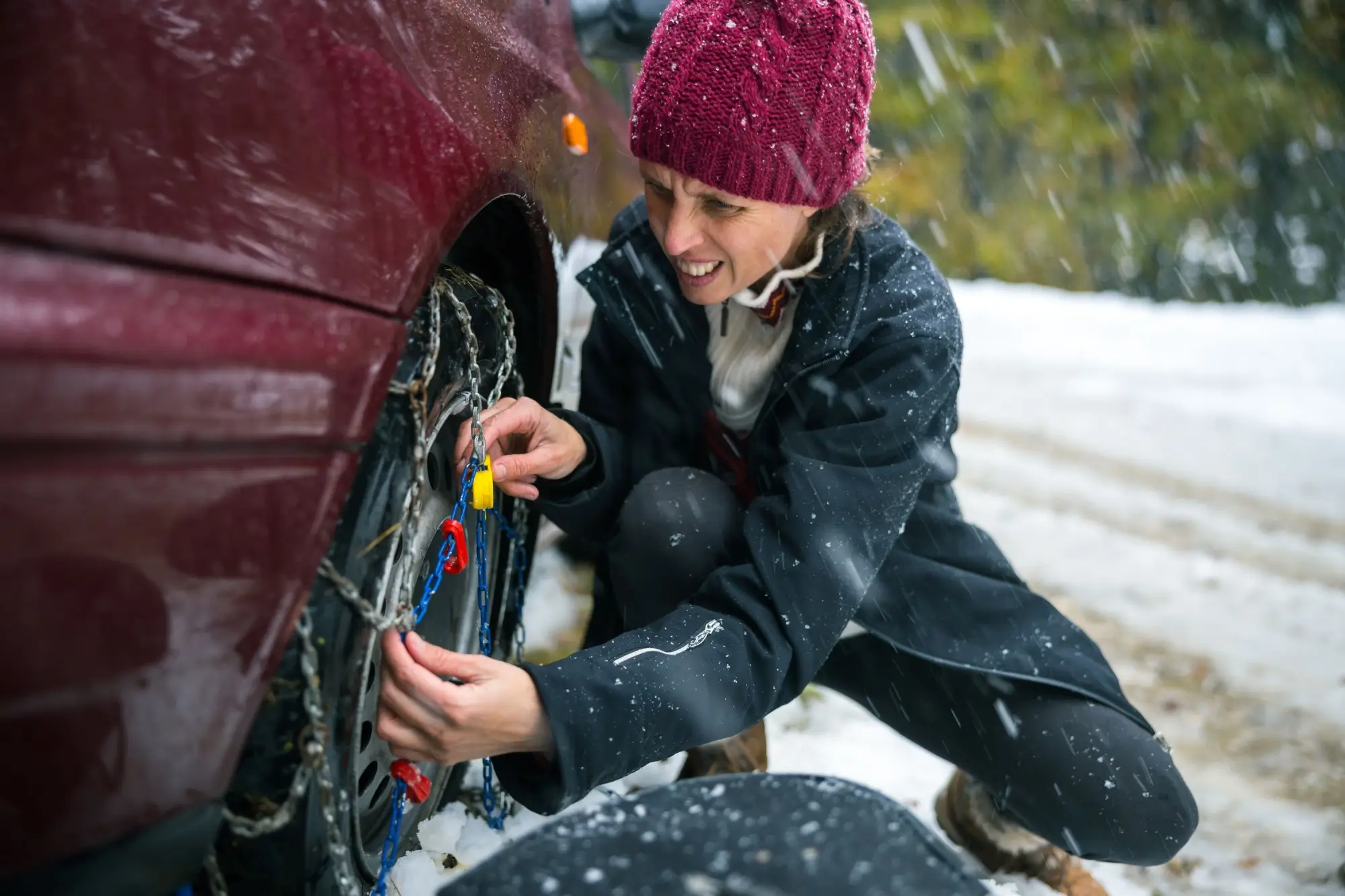 - MotorGuru.cz Mladá žena při nasazování klasických ocelových sněhových řetězů.